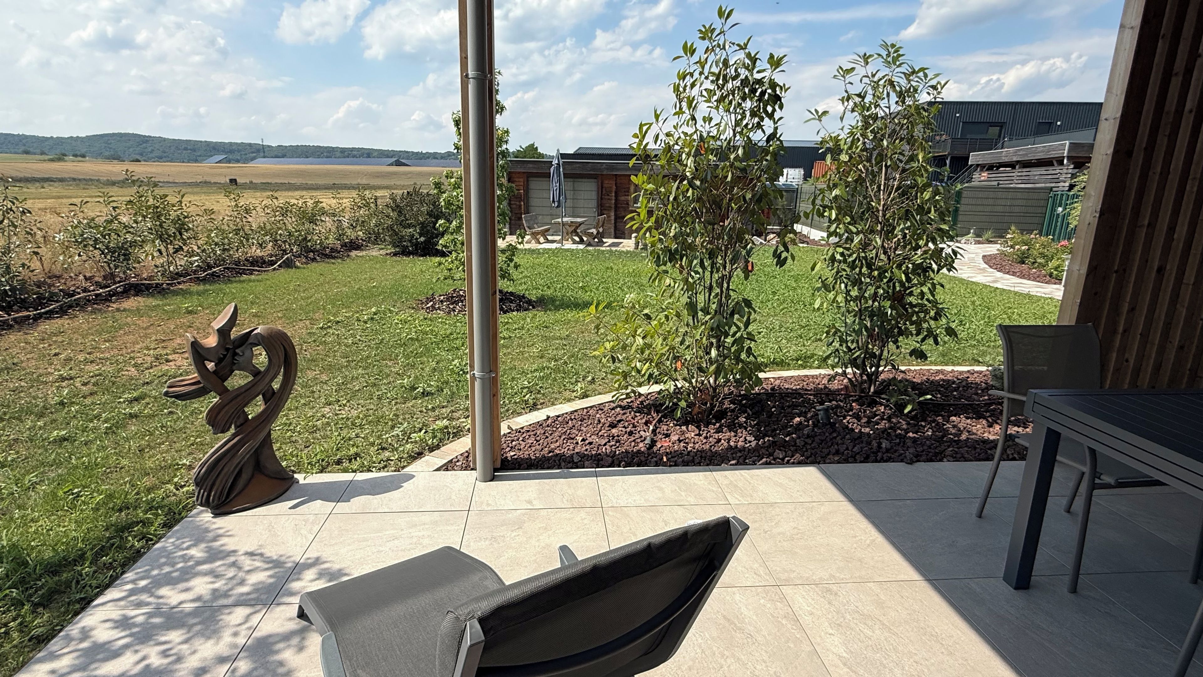 Een terras met tuinmeubilair, een beeld en uitzicht op een gebouw en het landschap.
