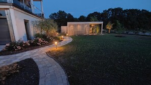 A modern outdoor area with a paved walkway, a wooden structure, and a well-maintained lawn. - Osmose Spa Lodge (Ingwiller)