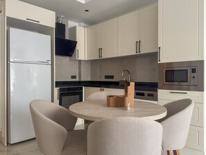 A modern kitchen with white cabinets, a stainless steel refrigerator, a built-in oven, a microwave, and a round table with four chairs.