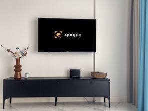 A modern living room with a flat-screen TV mounted on the wall displaying the Google logo, a black console table with a vase of dried flowers, and a woven basket.
