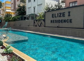 En swimmingpool med et skilt, der viser 'ELIZE I RESIDENCE', og en bygning i baggrunden.