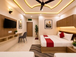 Ein modernes Hotelzimmer mit Flachbildfernseher, Schreibtisch, einem Bett mit rot-weißer Bettwäsche und Deckenventilator.