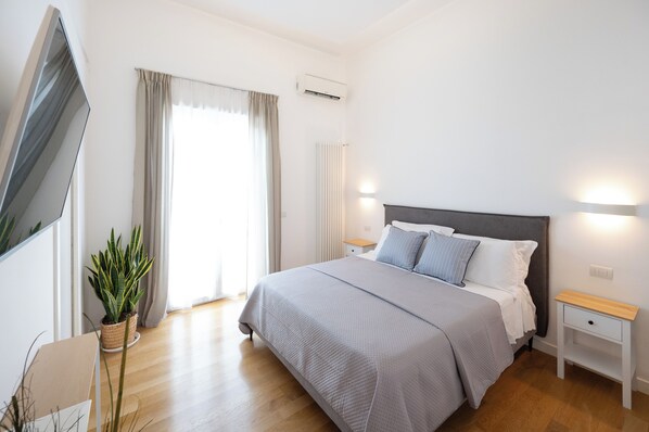Ein Schlafzimmer mit einem Bett, Nachttischen, einer Zimmerpflanze und einem Fenster mit Vorhängen.