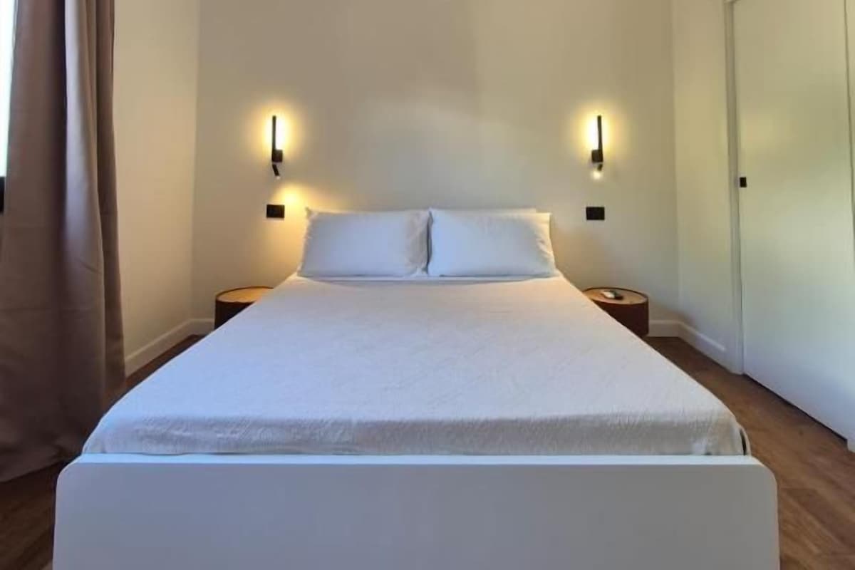 A bedroom with a single bed, two bedside tables, a nightstand, and a door.