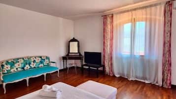 A hotel room with a bed, a sofa, a TV, and a window with curtains.