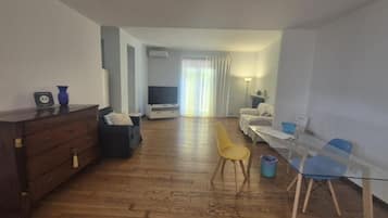 Habitación de hotel con piso de madera, un sofá, televisor, lámpara y una pequeña mesa con sillas.