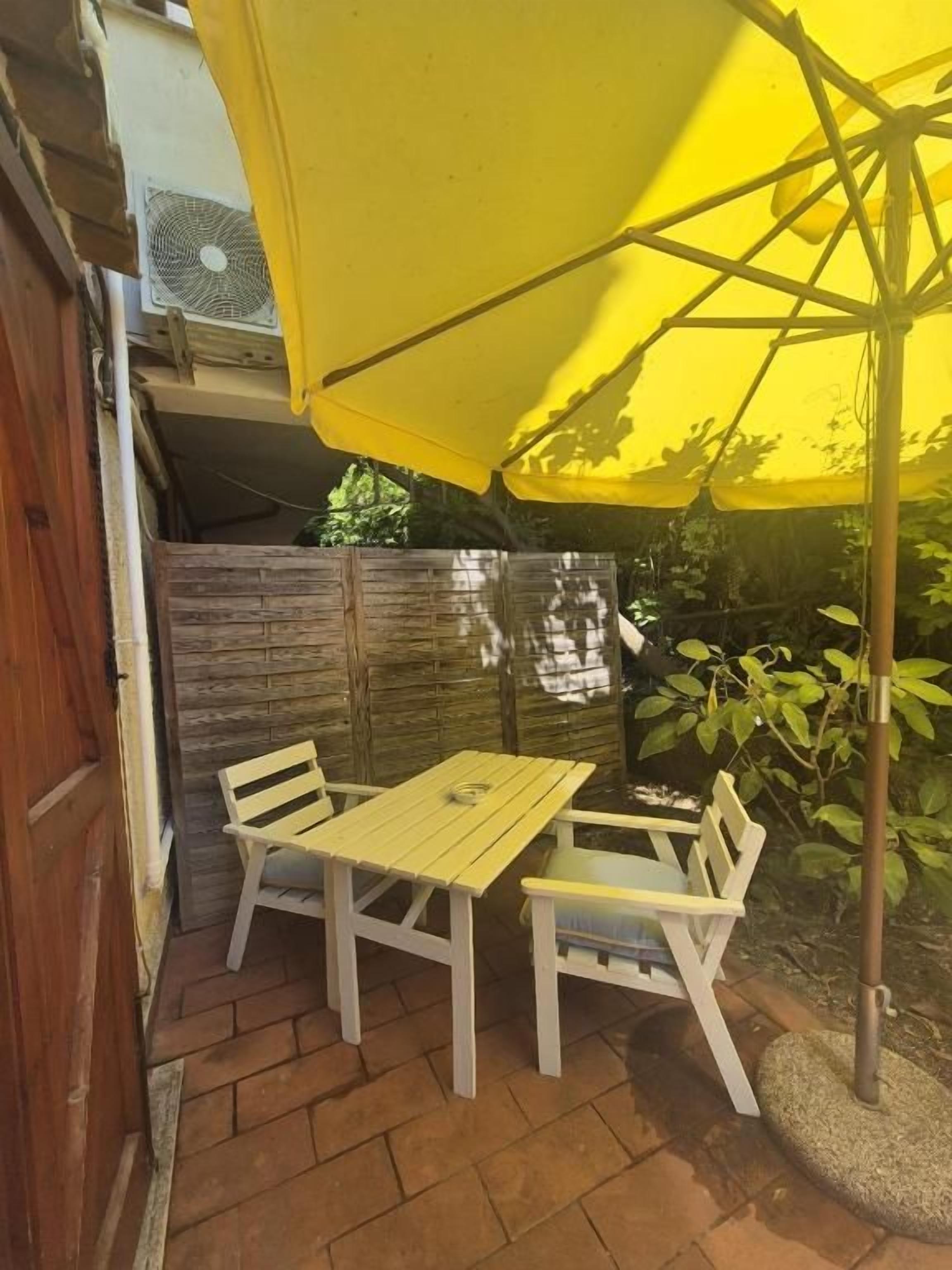 An outdoor patio with a yellow umbrella, a wooden table, and two chairs.