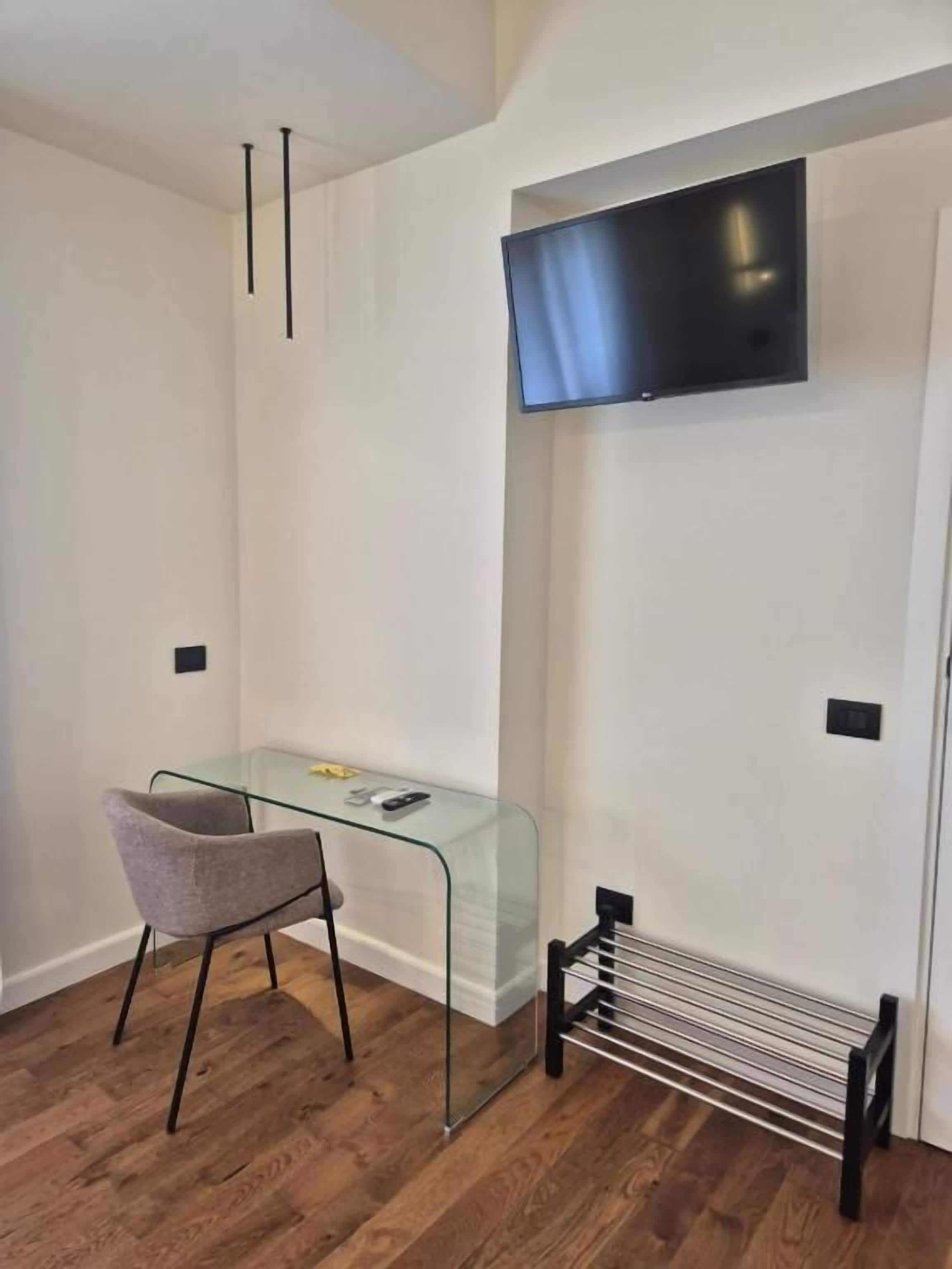 Une pièce comprenant un bureau en verre, une chaise, un téléviseur à écran plat fixé au mur et un radiateur.