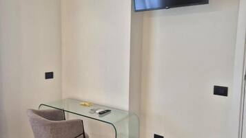 Une pièce comprenant un bureau en verre, une chaise, un téléviseur à écran plat fixé au mur et un radiateur.