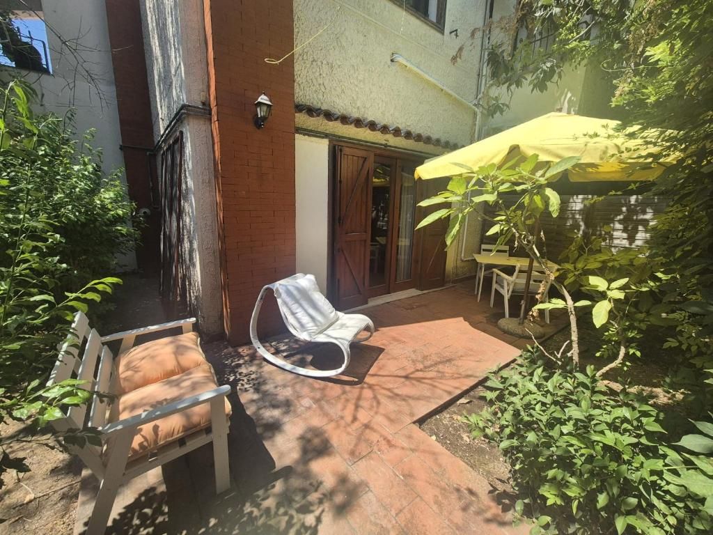 An outdoor patio with a white chair, a yellow umbrella, and a brick wall.