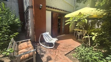 An outdoor patio with a white chair, a yellow umbrella, and a brick wall.