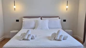 Ein Bett mit weißer Bettdecke, zwei Nachttischlampen und ordentlich gefaltete Handtücher.