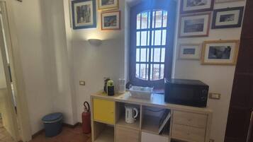 A room with a window, a microwave, a small cabinet, and a trash bin.