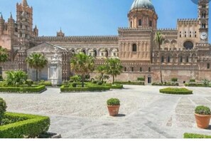 A historic building with a large central dome, arched windows, and a symmetrical courtyard with palm trees and potted plants. - A due passi da... (Napoli)