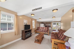 A living room with a television, sofa, and a fireplace. There are windows with curtains and a sign on the wall. - The Salty Escape (Narragansett)