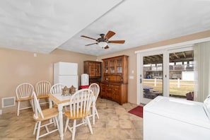 A dining area with a table and chairs, a ceiling fan, and a view of the outside through a glass door. - The Salty Escape (Narragansett)