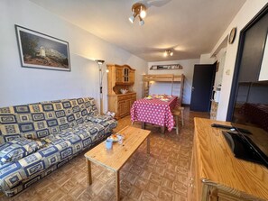 A furnished living room with a sofa, a dining table with a red tablecloth, a wooden cabinet, and a kitchen area with a bunk bed. - 50m from ski slopes, 7th floor, balcony, tv, ski locker, 53m², Vars (Vars)