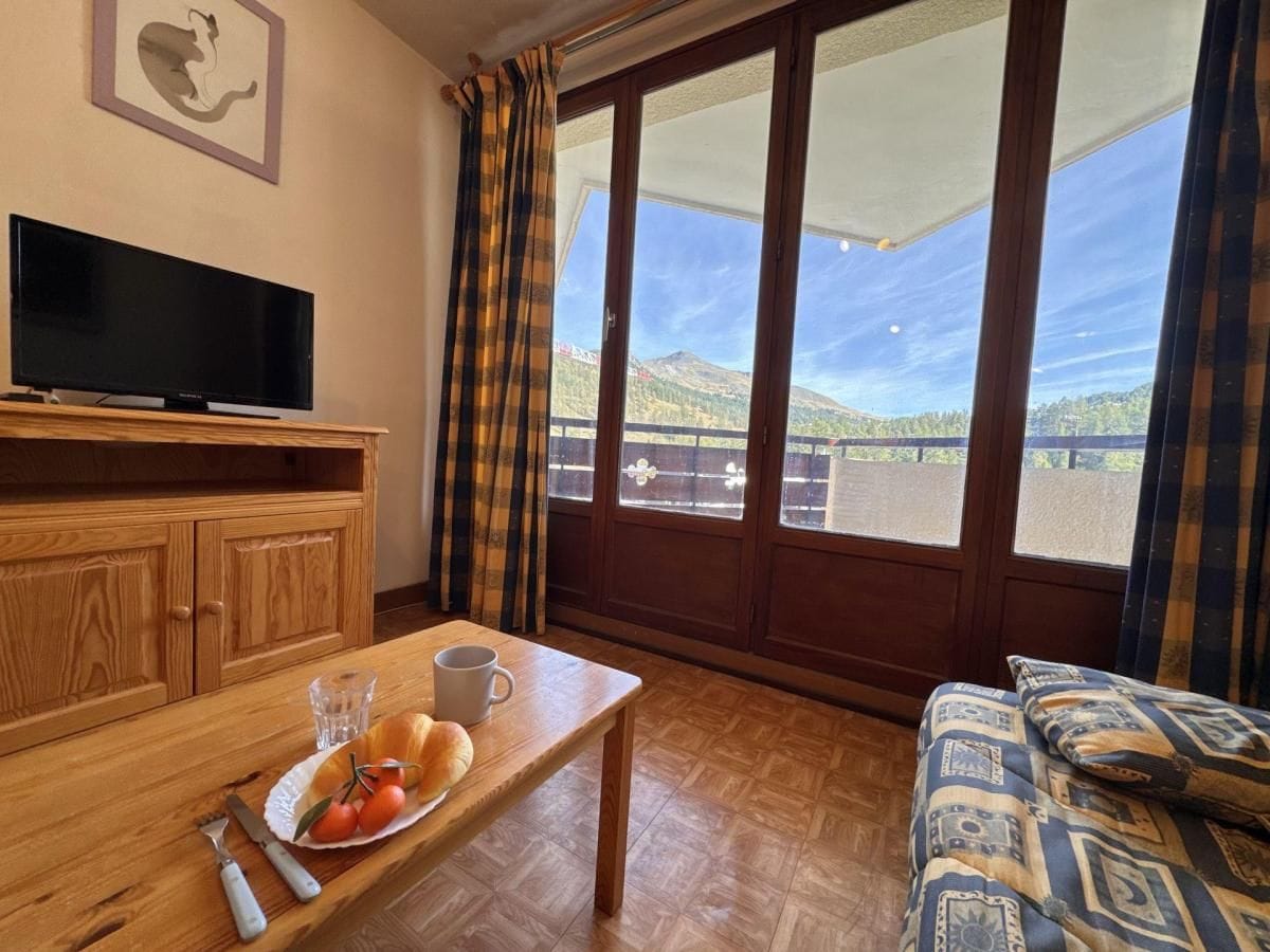 A room with a wooden table, a television, a sofa, and a view of a mountain landscape through large windows.