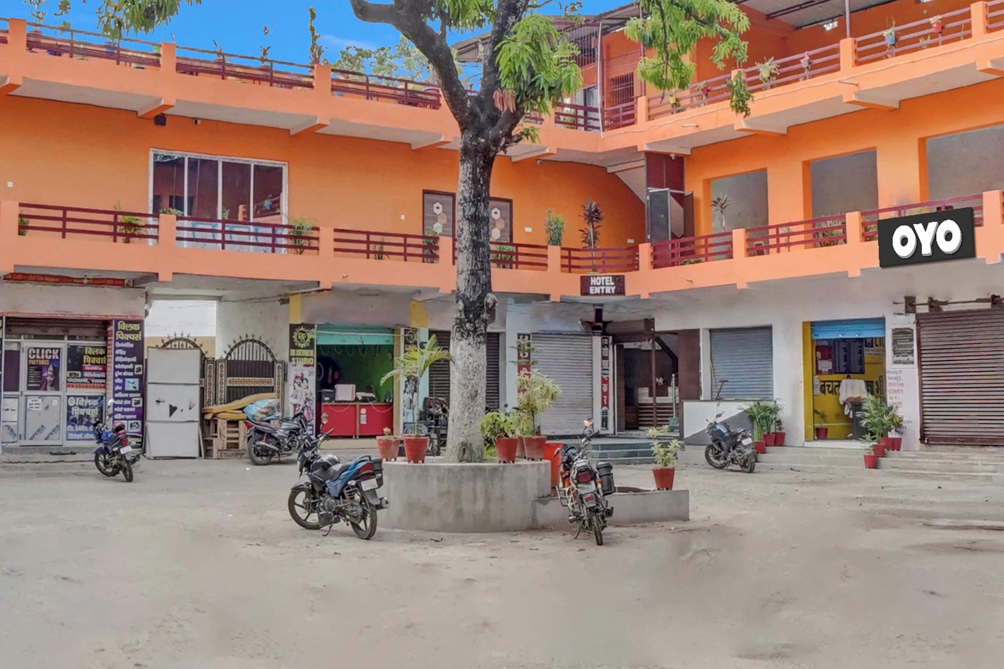 Un immeuble à plusieurs étages, avec une enseigne indiquant l’entrée de l’hôtel « OYO », plusieurs motos garées et des plantes en pot.