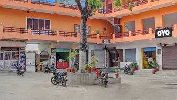 Un immeuble à plusieurs étages, avec une enseigne indiquant l’entrée de l’hôtel « OYO », plusieurs motos garées et des plantes en pot.