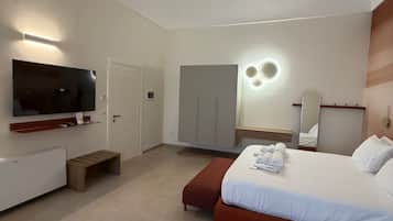 Ein modernes Hotelzimmer mit Fernseher, Kleiderschrank, einem Bett mit Handtüchern und einer kleinen Sitzecke.