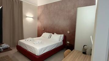 Habitación de hotel con cama, escritorio, silla, espejo y lámpara de pared.