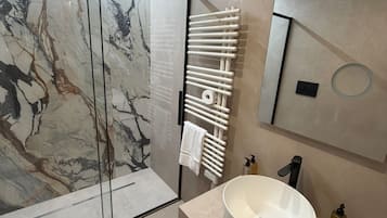 Ein modernes Badezimmer mit Duschkabine aus Glas, einem weißen Waschbecken mit schwarzem Wasserhahn und einer Marmor-Spritzschutzwand.