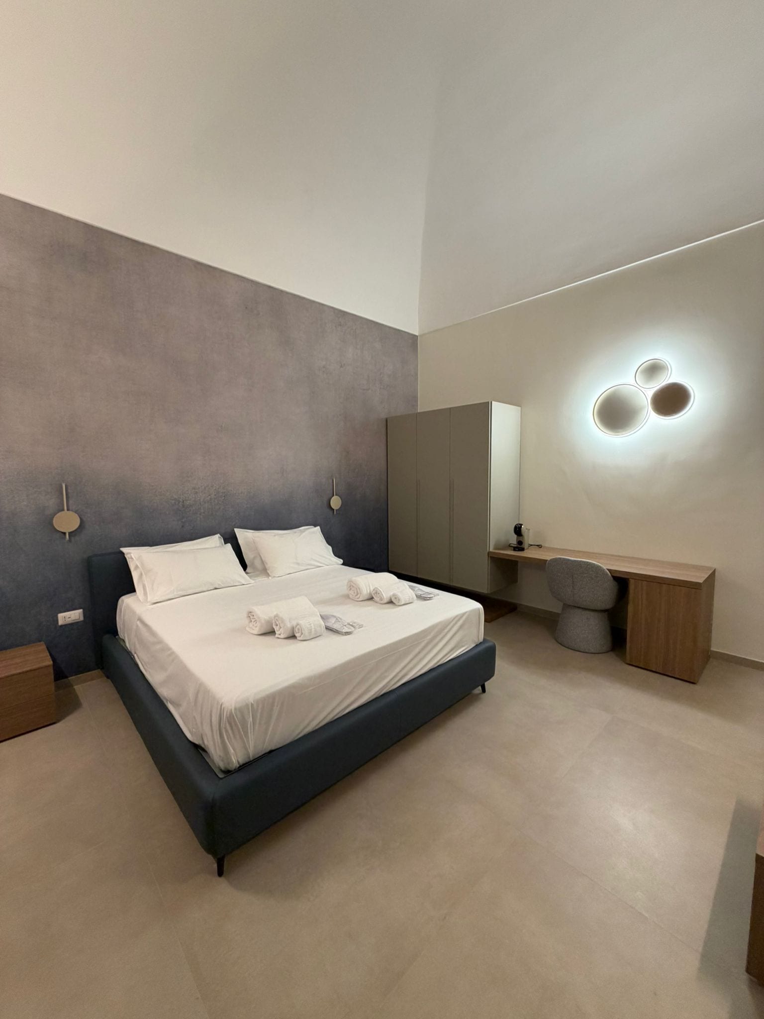 A modern bedroom with a large bed, bedside tables, a desk, and a mirror.