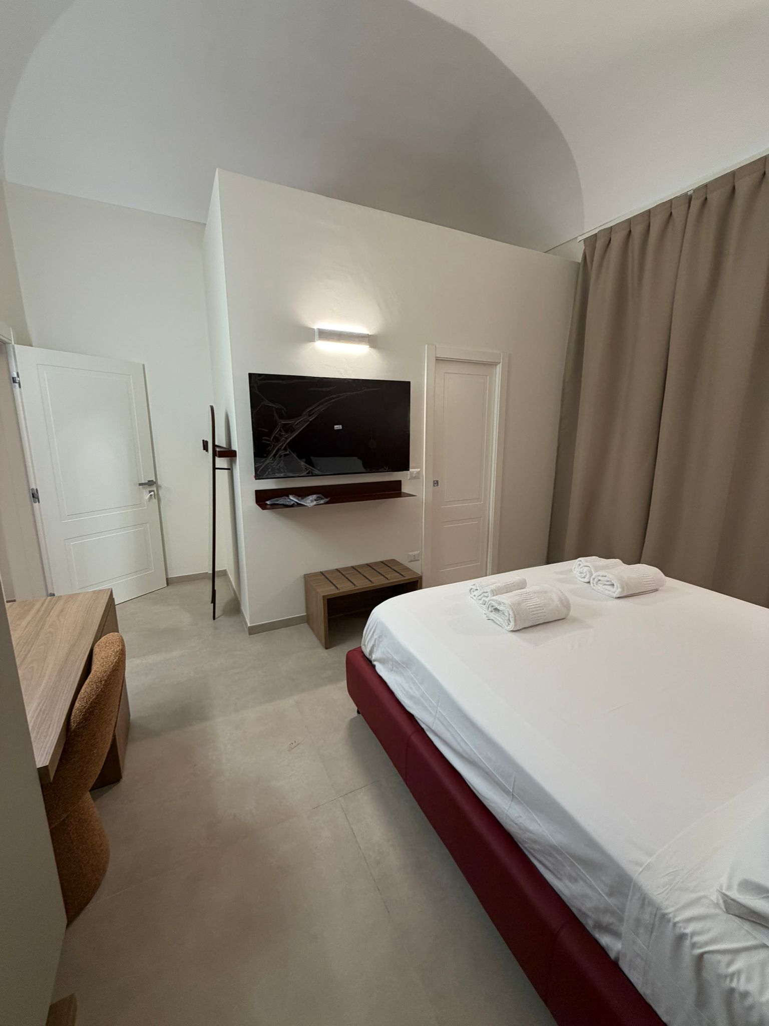 Een hotelkamer met een bed, een aan de muur bevestigde televisie, een bureau en een deur.