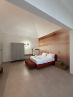 Un dormitorio moderno con una cama grande, un banco, un armario e iluminación empotrada en la pared.