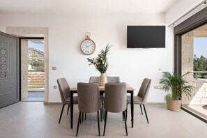 Ein stilvoller Essbereich mit Tisch, Stühlen, einer Blumenvase, einer Wanduhr und einem Fernseher.