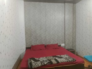 Quarto individual com parede estampada, colcha vermelha e manta com estampa de leopardo.
