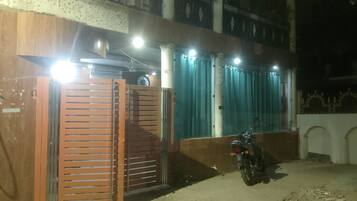 A gated entrance with a motorcycle parked inside, a clock on the wall, and a building with a balcony.