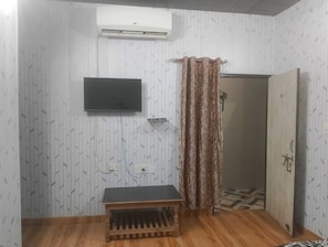 Quarto com televisão de tela plana na parede, um banco de madeira, cortina estampada e porta com o número 102.