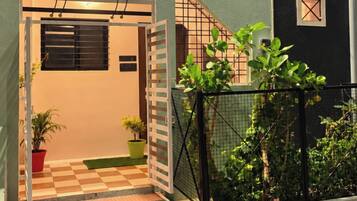A residential building with a gated entrance, a staircase leading to the entrance, and a small garden area with potted plants.