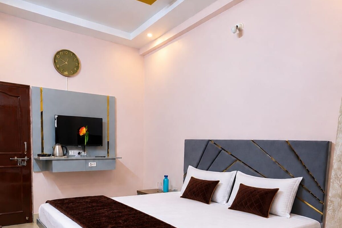 A bedroom with a bed, a ceiling fan, a mounted TV, and a clock on the wall.