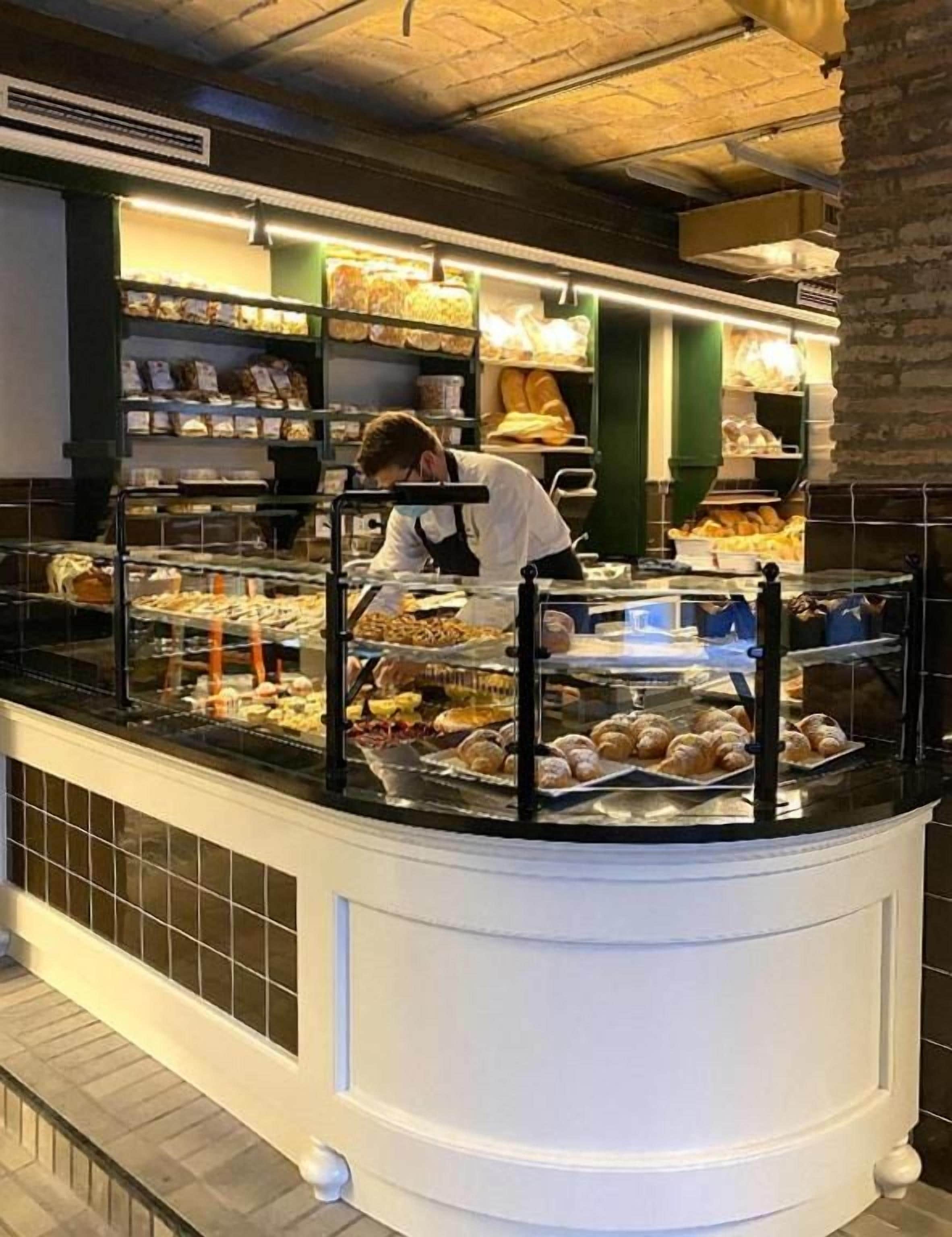 Mostrador de panadería con pasteles y una persona trabajando detrás.