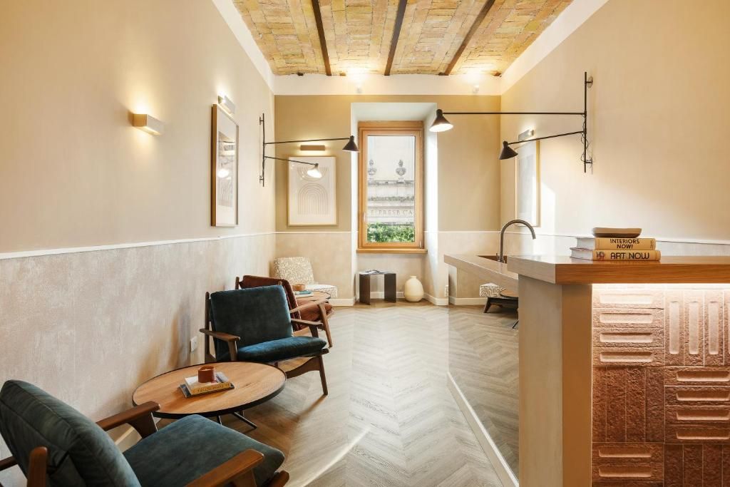 Un hall de hotel con piso de espiga, zona de estar con sillas y una mesa, mostrador de recepción y obras de arte enmarcadas en las paredes.