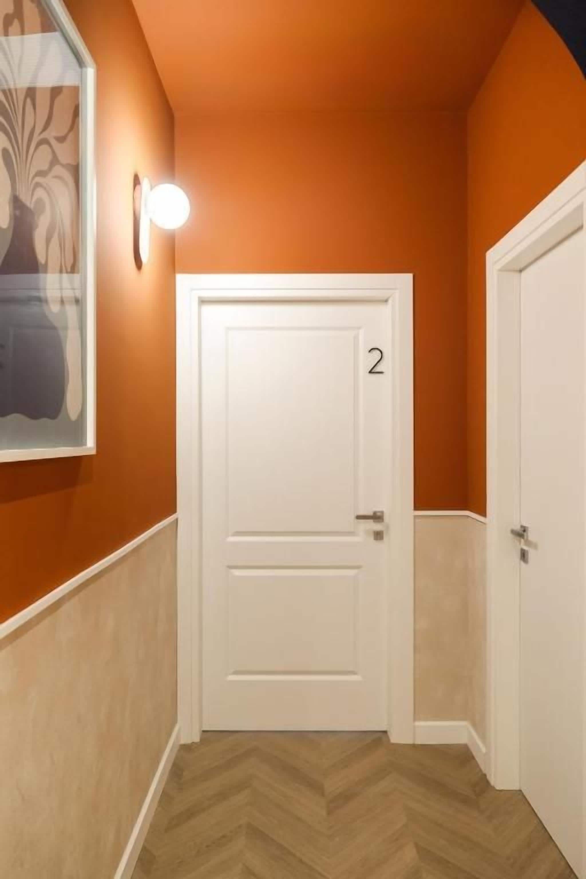 Un pasillo con una puerta blanca marcada con el número 2, un accesorio de iluminación en la pared y un suelo con estampado de tablero de ajedrez.