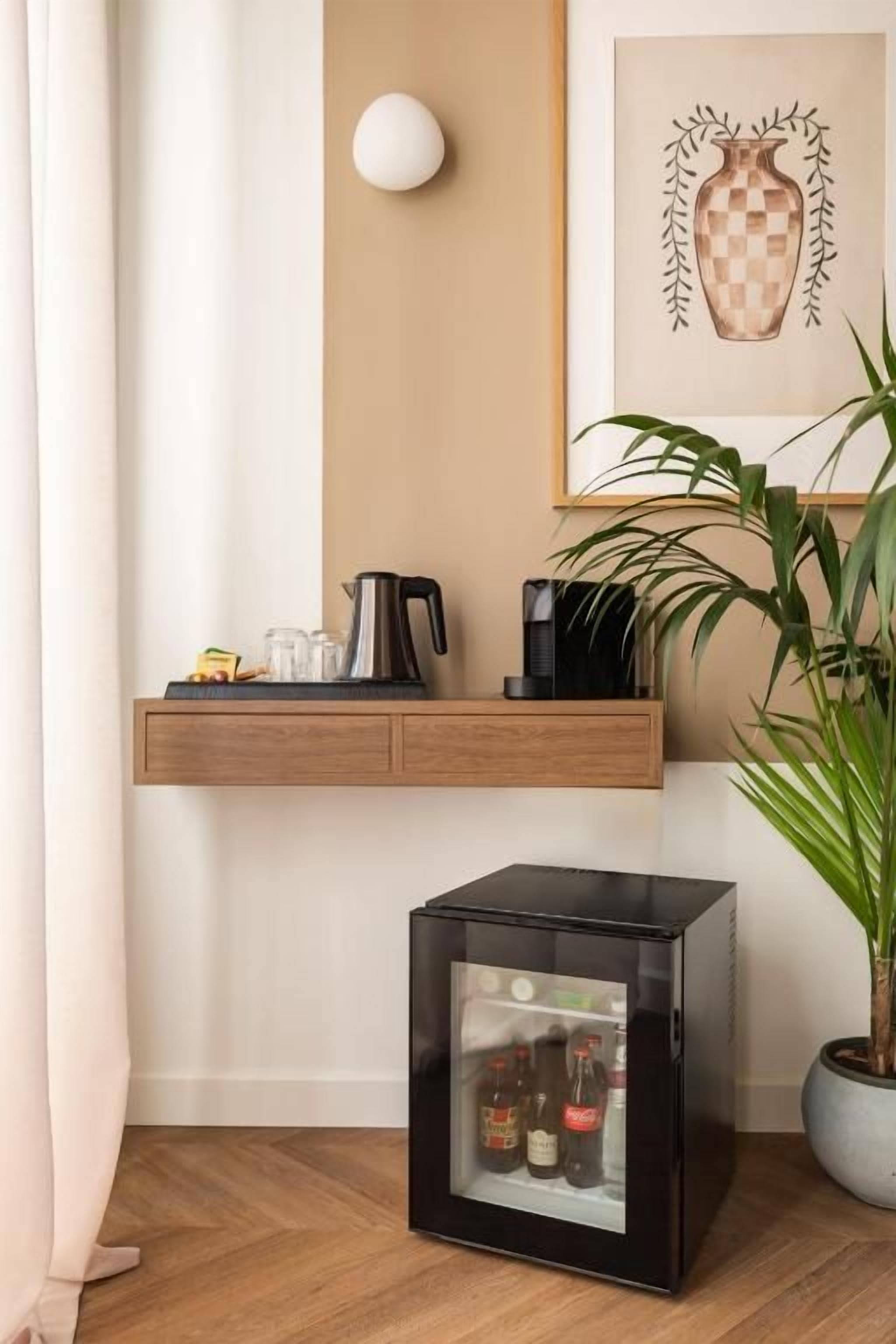Una habitación con un estante de madera que contiene una cafetera y tazas, un armario negro con botellas y una planta en maceta.