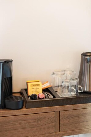 Una estación de café con una cafetera, una caja de té Earl Grey y varios vasos de vidrio sobre una encimera de madera.