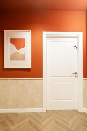 Una puerta blanca con el número 6, una obra de arte abstracta enmarcada en la pared y un suelo con patrón de espiga.