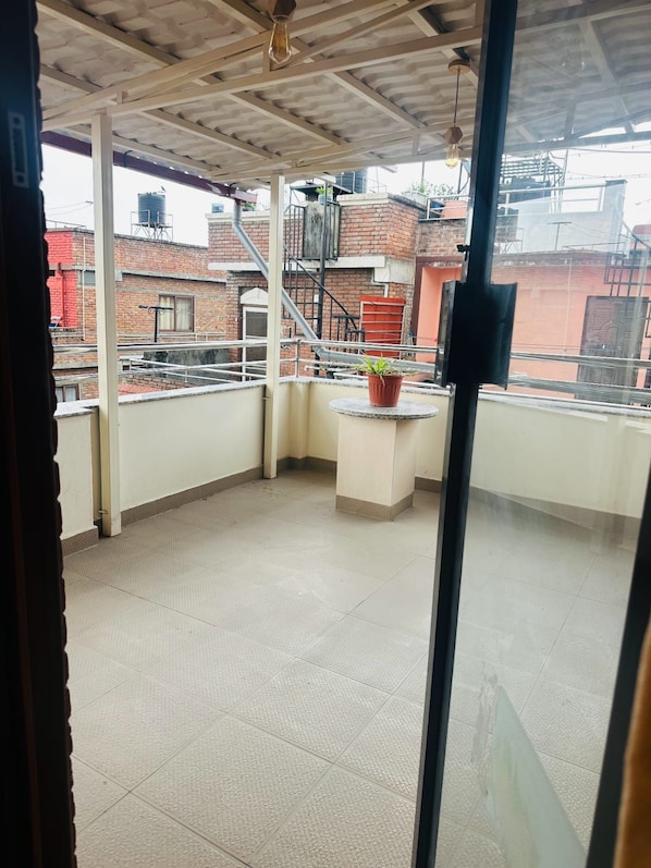 Ein Balkon mit einem Blumentopf, gefliestem Boden und Blick auf Gebäude im Hintergrund.
