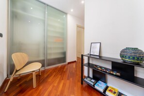A modern interior with a wooden floor, a glass door, a chair, and a black shelf with books and decorative items. - UR NEST San Felice - 140 sqm apartment with terrace and balcony in the historic center (Bologna)