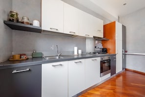 A modern kitchen with a stainless steel countertop, white and gray cabinets, a built-in oven, and a wooden backsplash. - UR NEST San Felice - 140 sqm apartment with terrace and balcony in the historic center (Bologna)