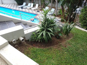 A swimming pool with a tiled deck, surrounded by lounge chairs and potted plants.