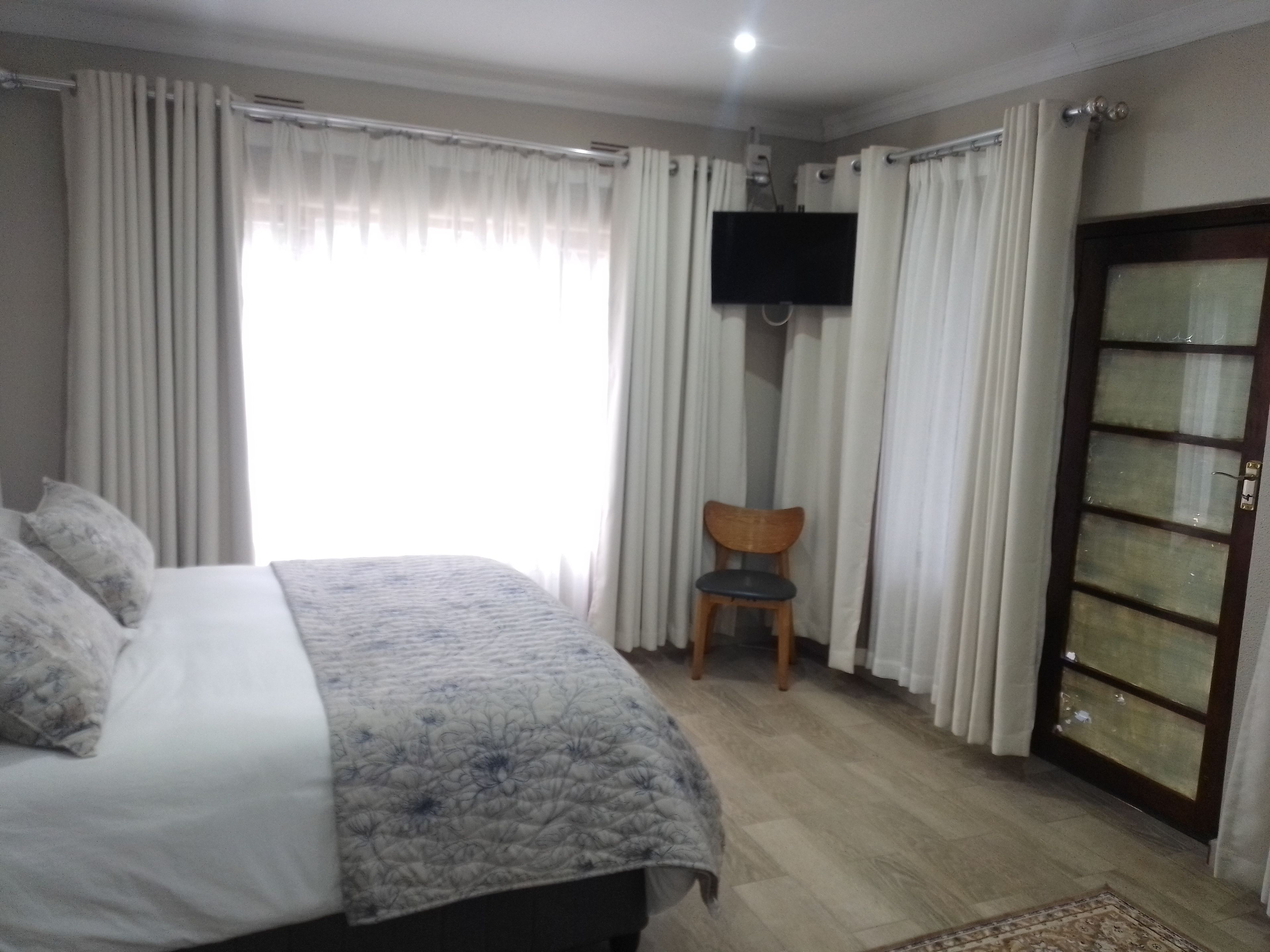 Une chambre à coucher avec un lit, des rideaux, une télévision, une chaise et une armoire.