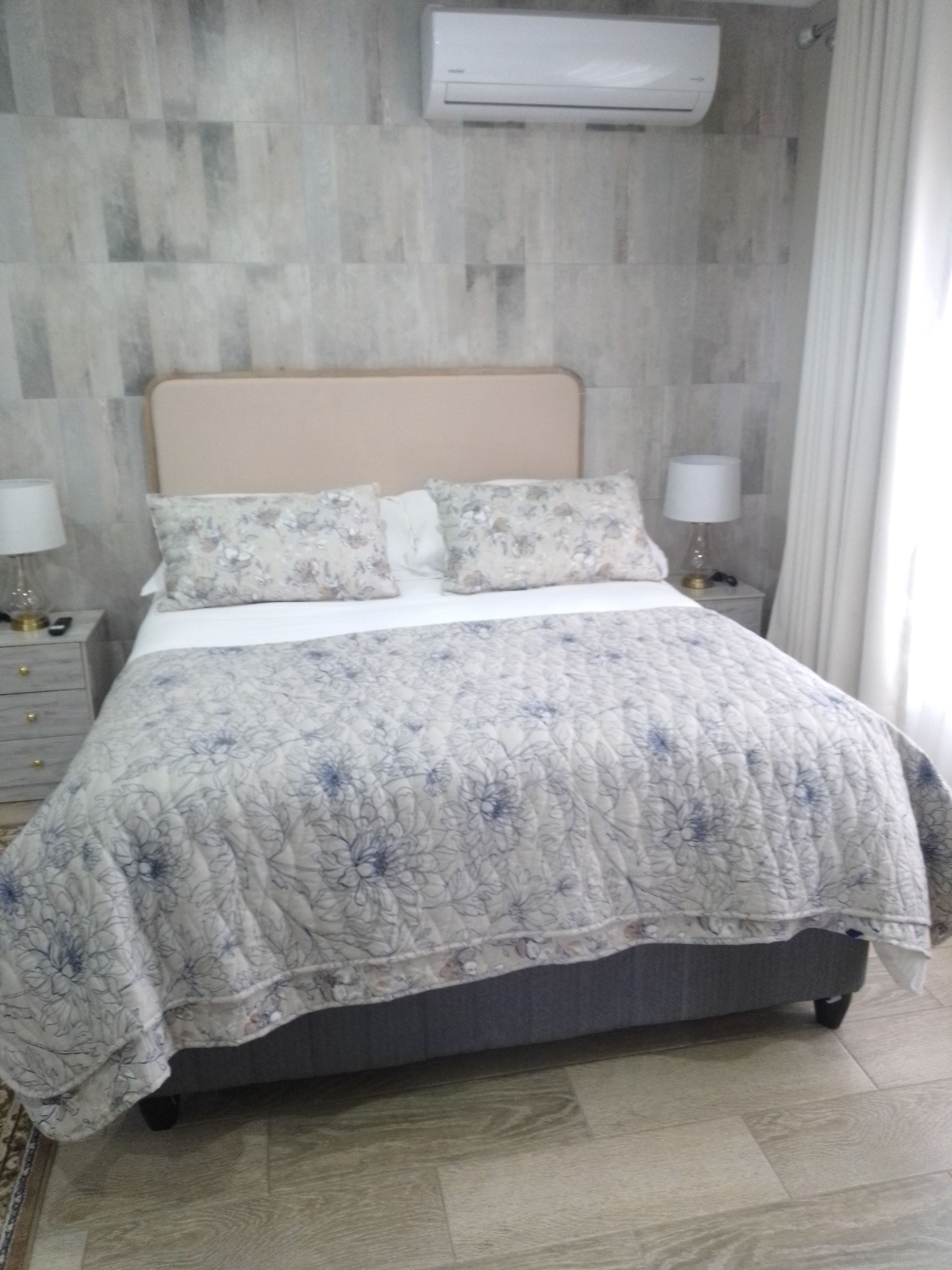 Un lit avec une couvre-lit à motifs floraux, une tête de lit et deux lampes de chevet.