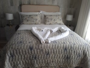 A neatly made bed with a floral-patterned duvet, two pillows, and a towel arranged on the bed.