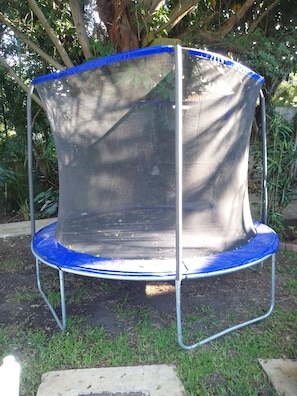 A trampoline with a safety net, surrounded by grass and trees.